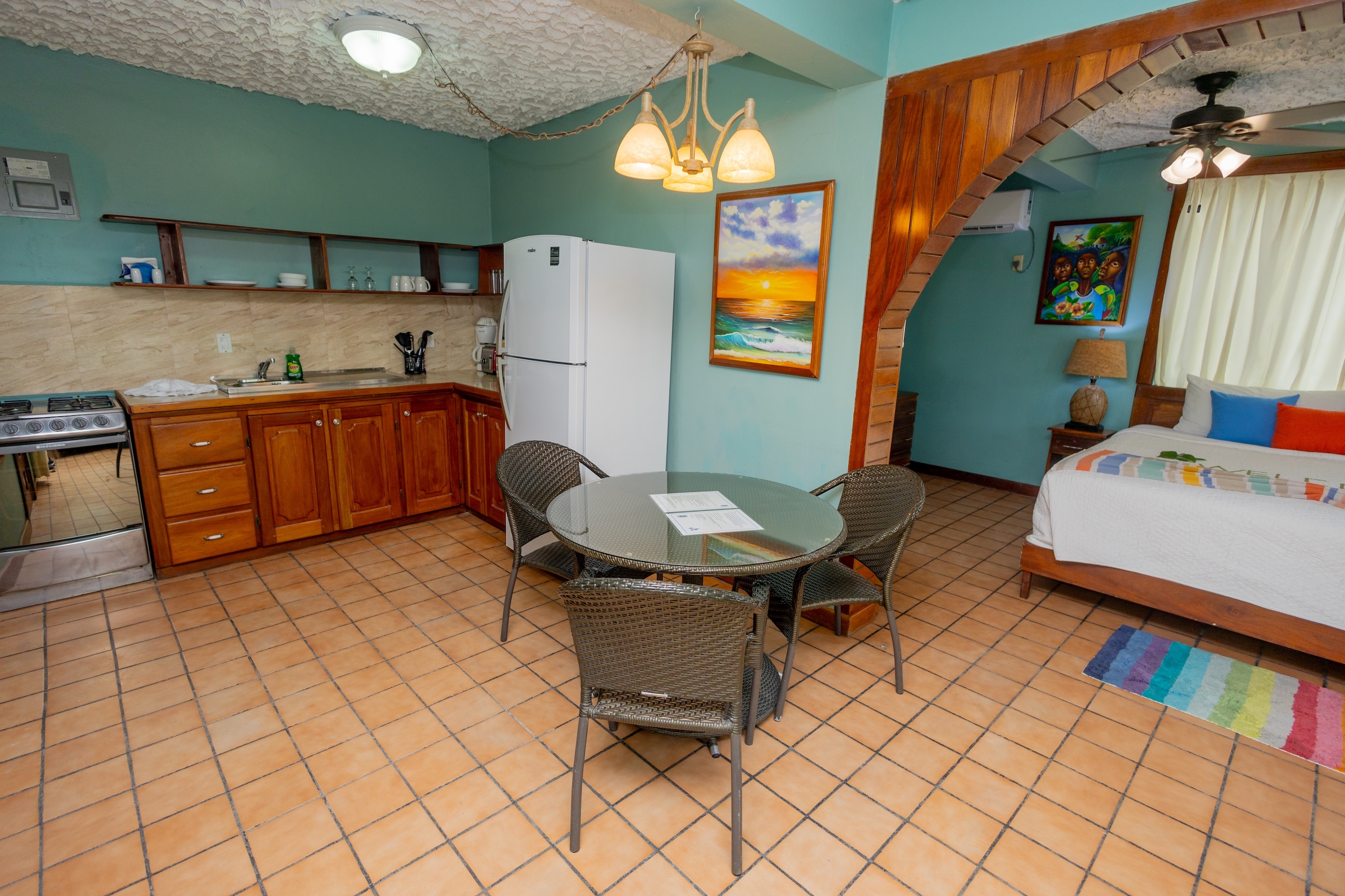 A studio apartment with teal walls, tiled floors, a kitchenette, a dining table with chairs, and a k