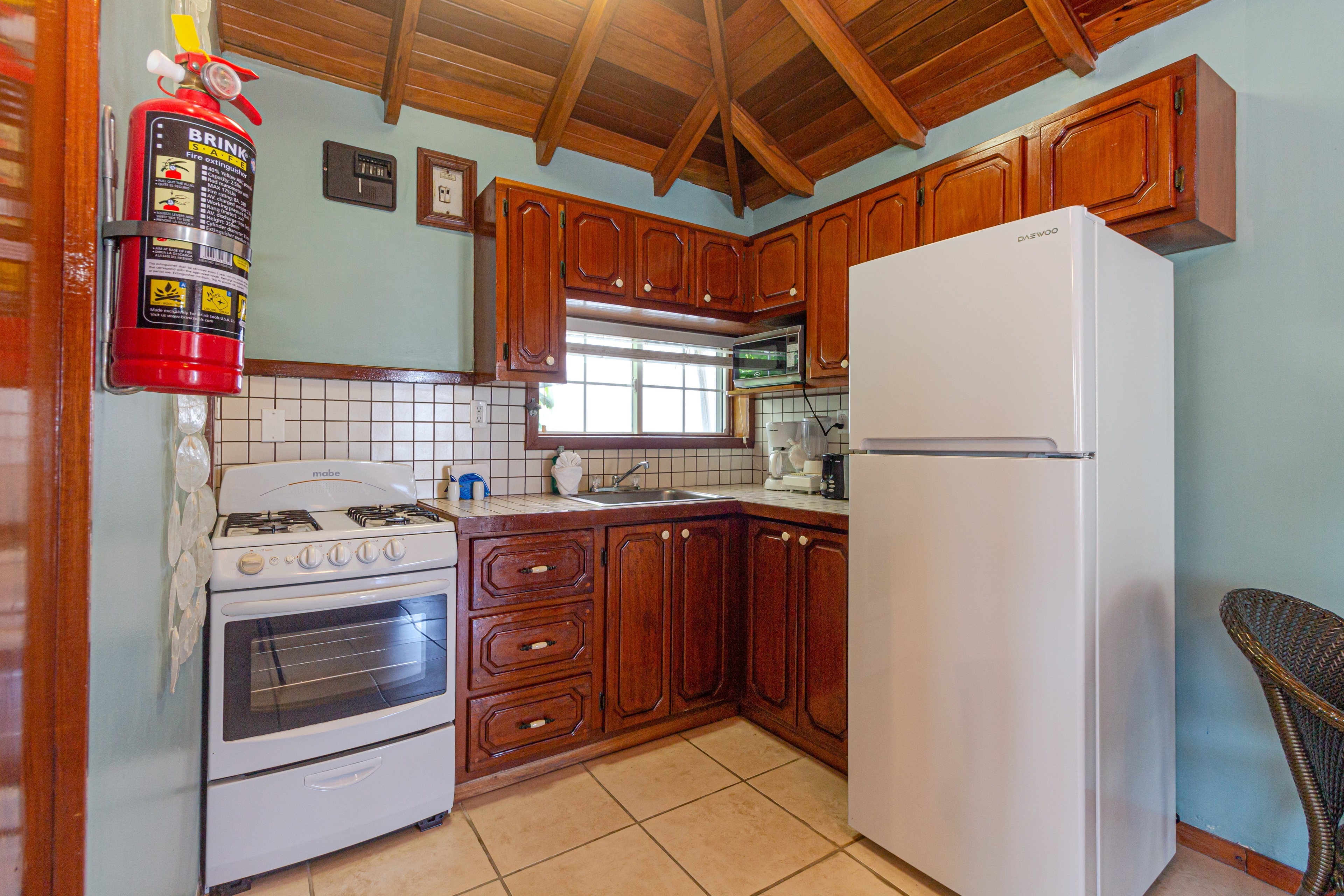 A compact kitchen with wooden cabinets, white appliances, light countertops, and a tiled backsplash.