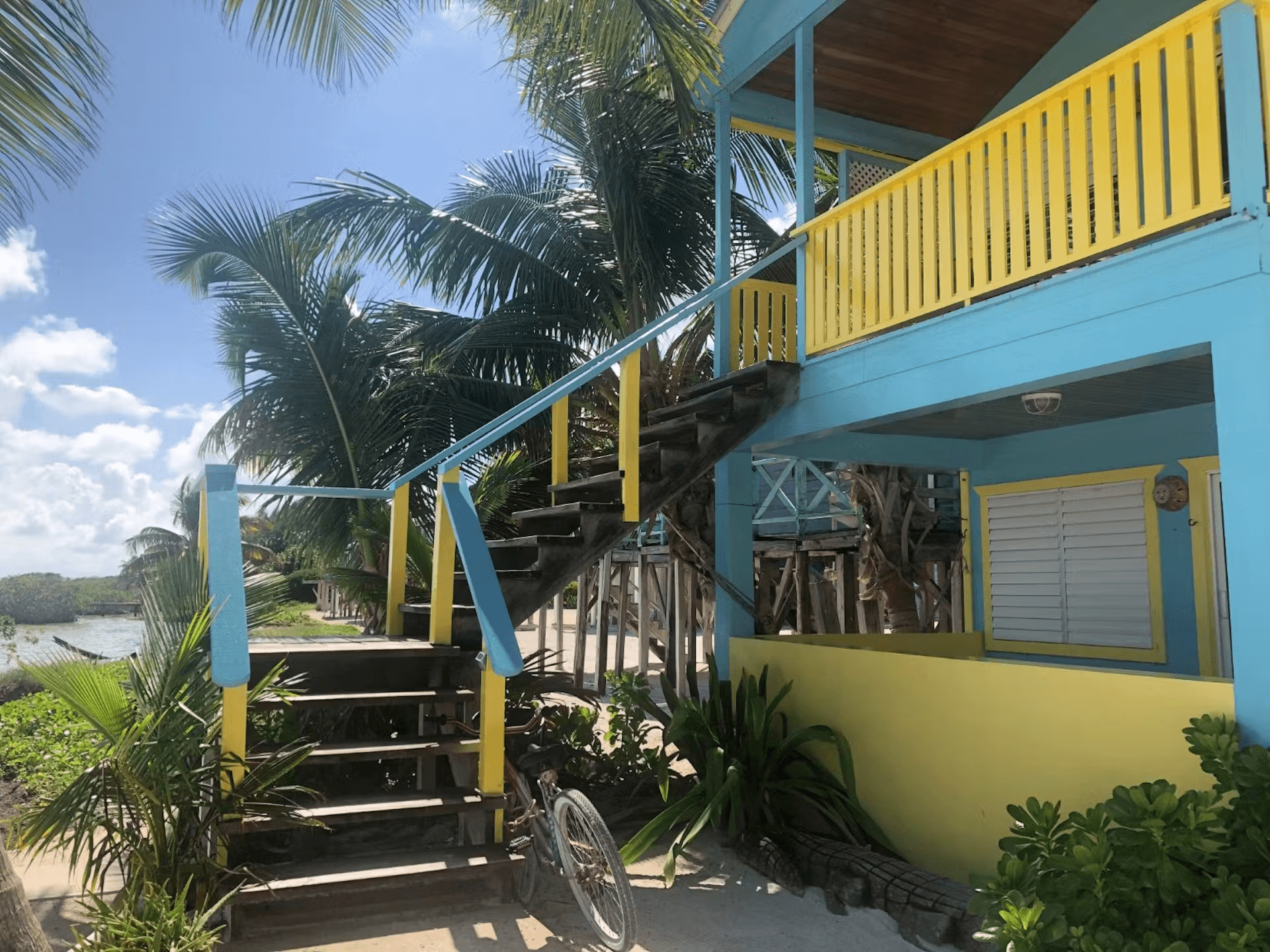 Exterior of a colorful blue and yellow cabana with stairs leading to second level, bright blue sky a