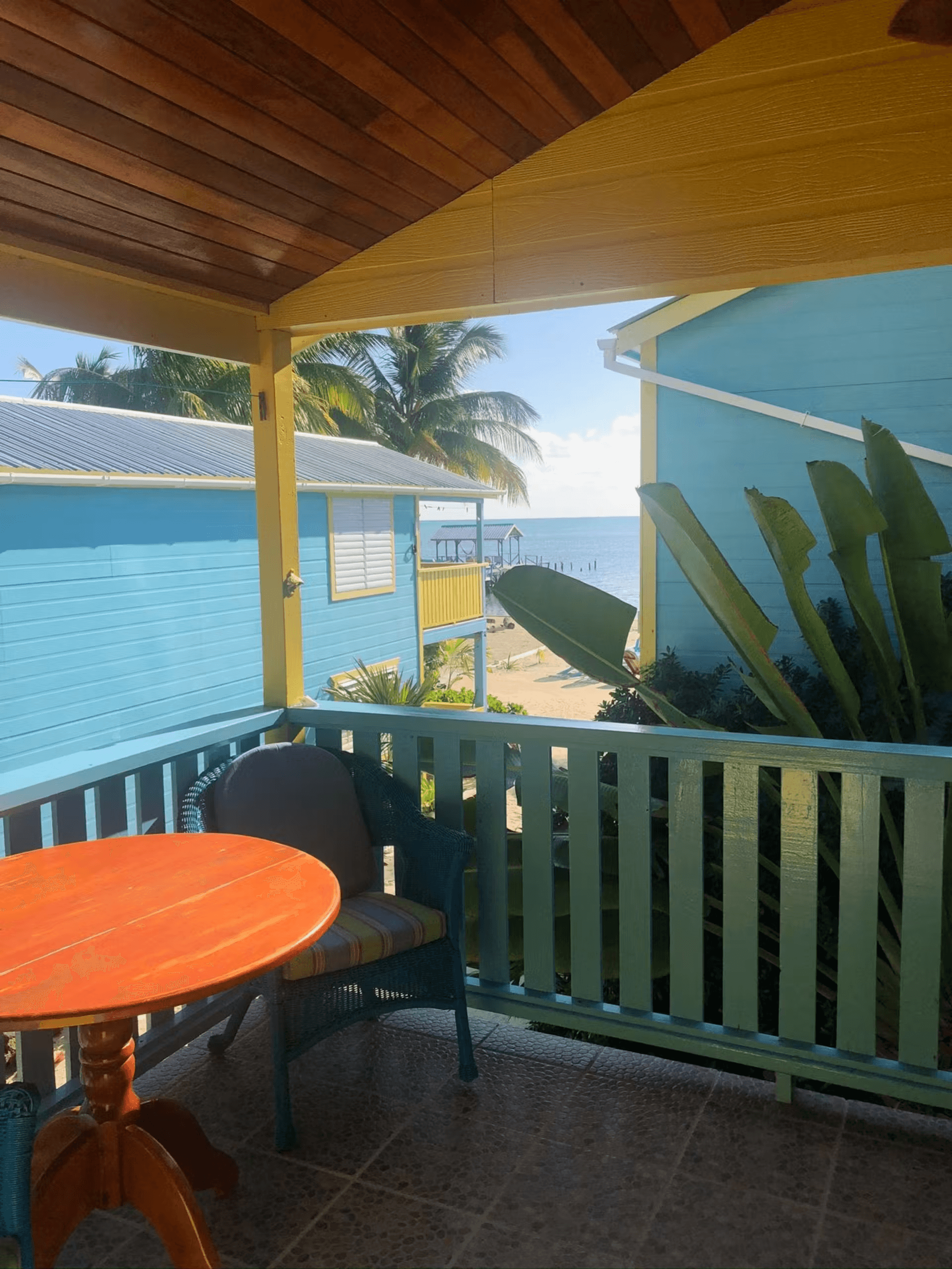 Balcony with cushioned chair and round table, view shows two other cabanas with the beach and ocean