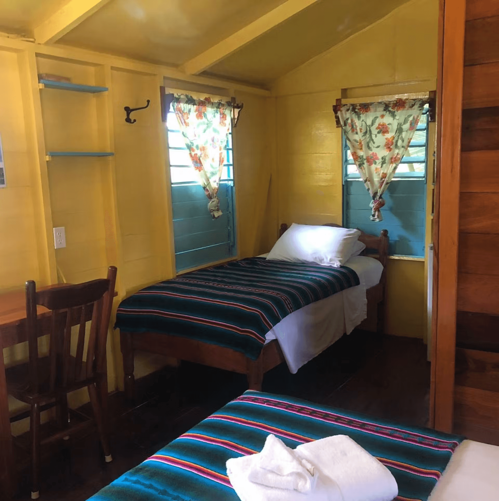Bedroom with yellow painted walls, showing foot of double bed with single bed in opposite corner, wo