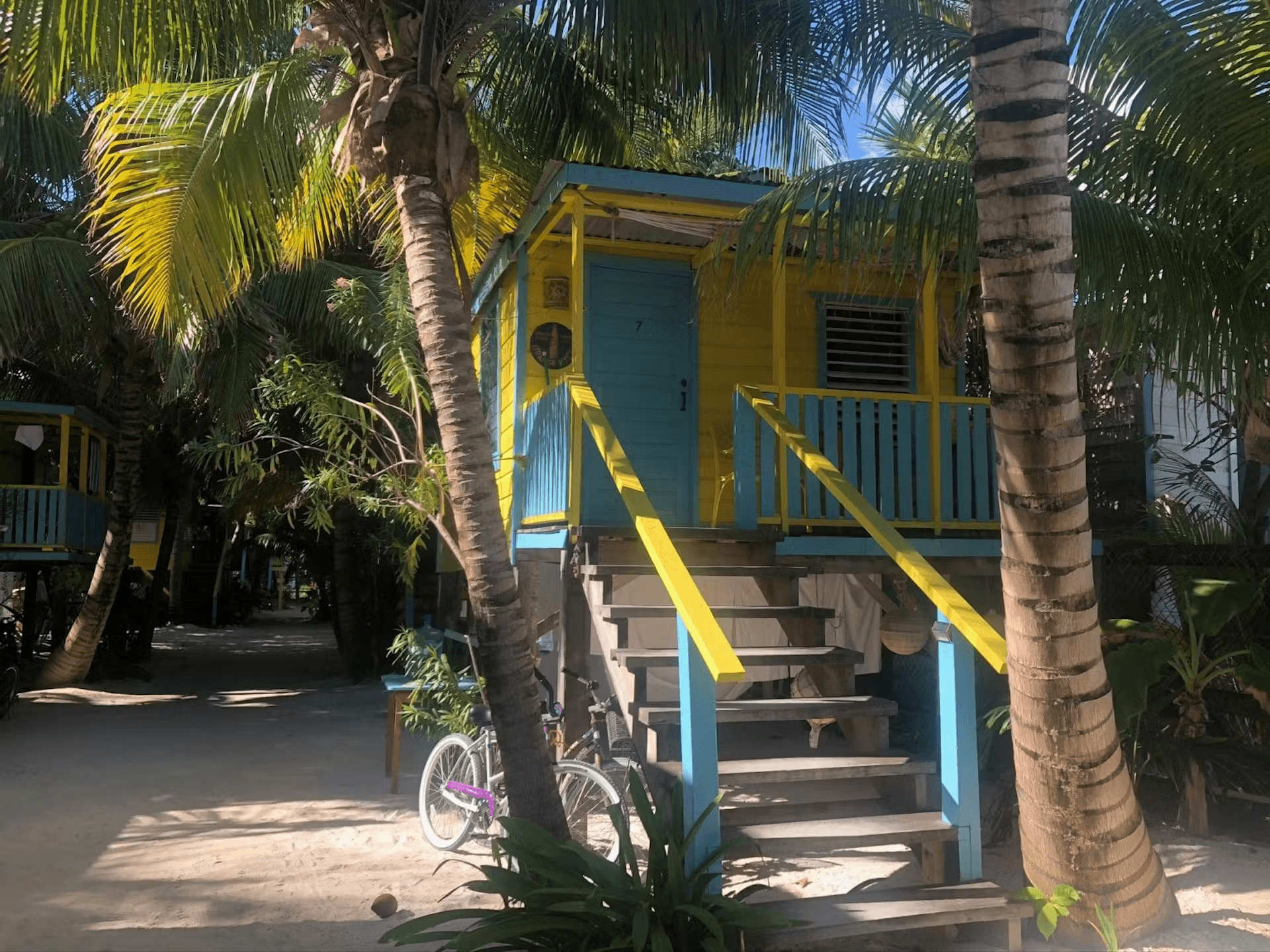 Exterior of a colorful blue and yellow cabana with stairs leading to second level and palm trees fla