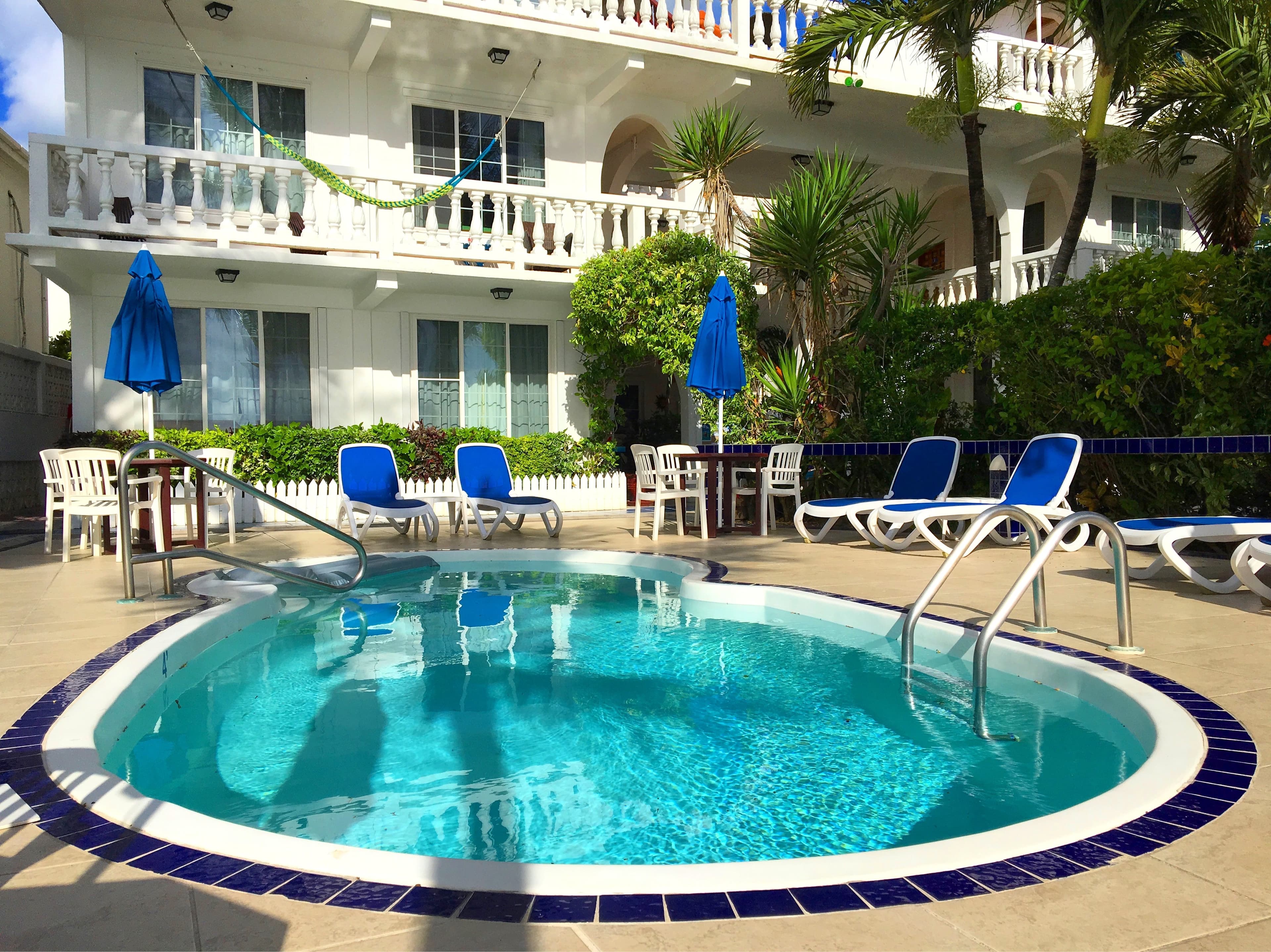 An oval swimming pool with blue and white tiling, surrounded by lounge chairs and umbrellas in front