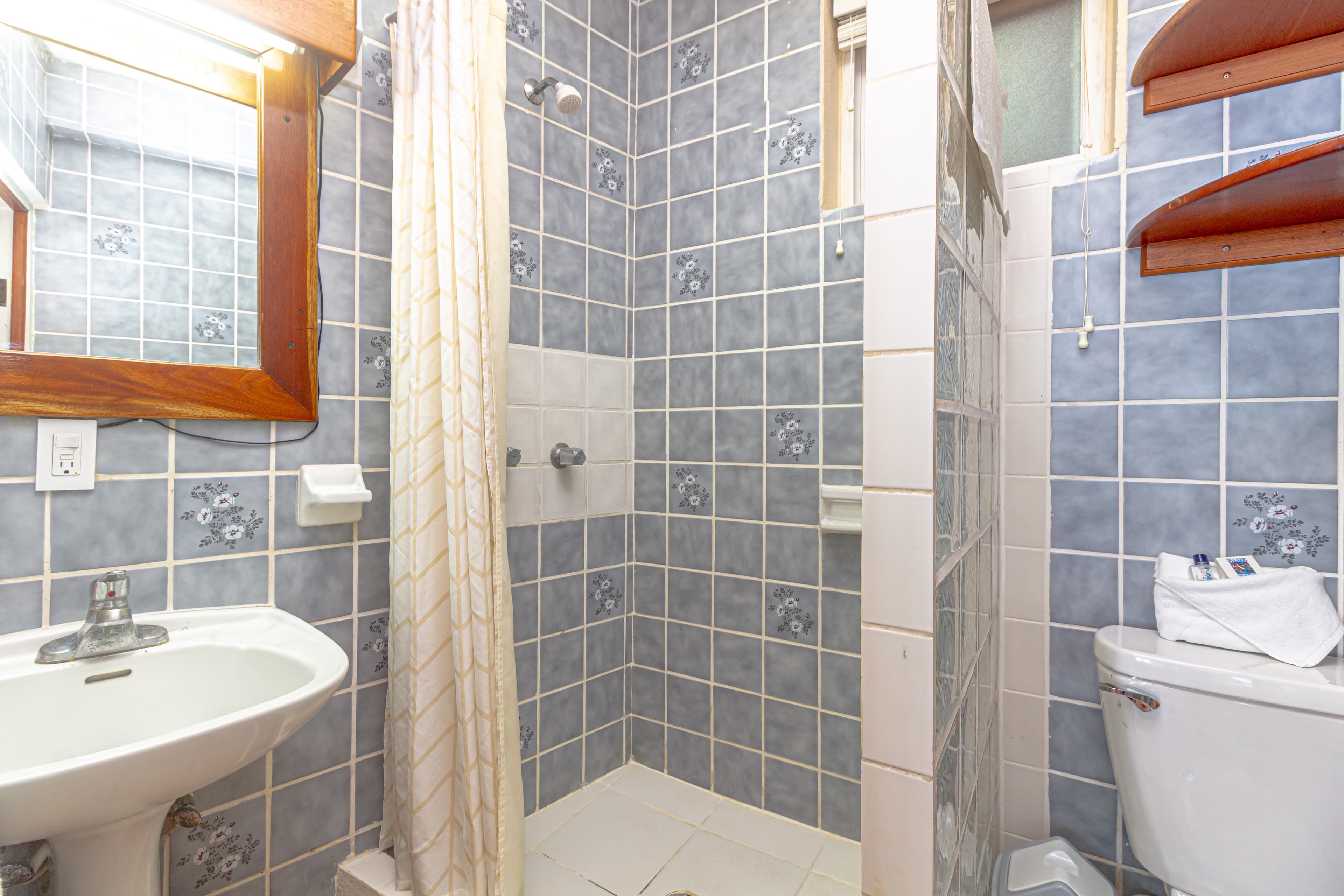 A compact bathroom with blue and gray patterned tiles, a wooden-framed mirror above a white sink, a