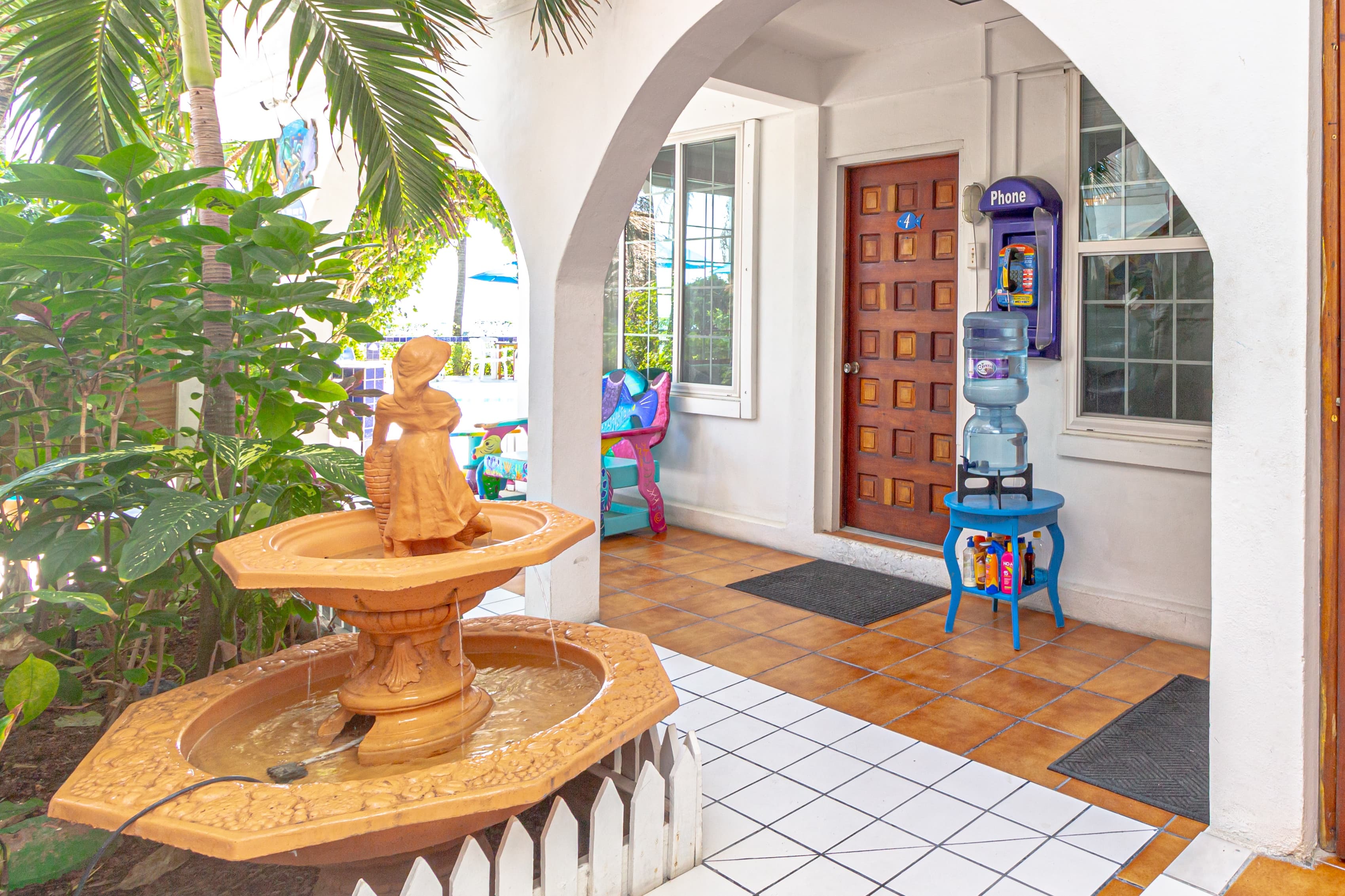 A covered outdoor entrance area with a tiered terracotta fountain, white arches, and a wooden door.