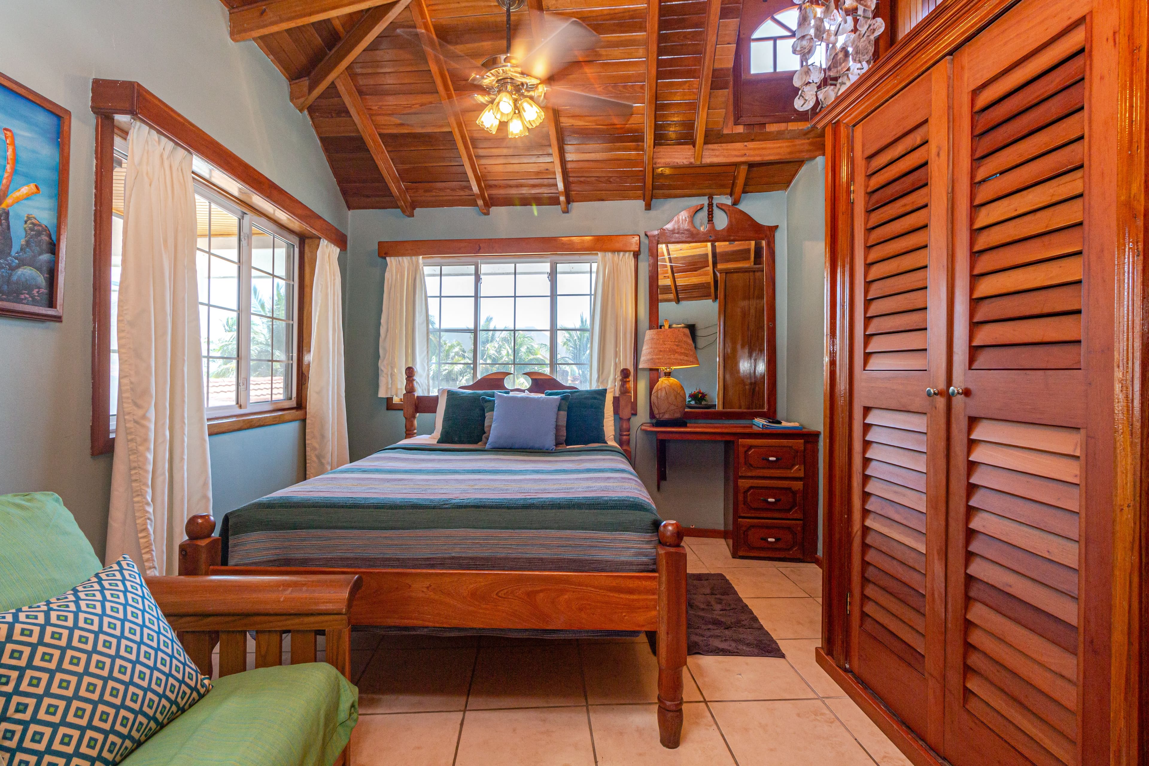 A room with a high wooden ceiling, a queen bed with blue bedding, a green futon, and a wooden wardro