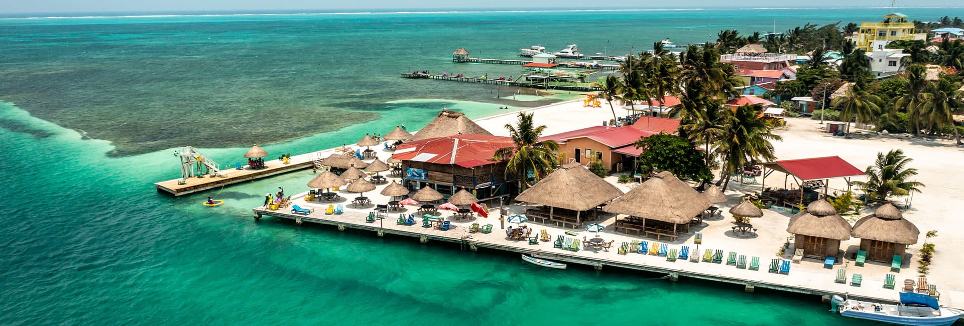 Aerial view of a tropical resort with thatched-roof structures and turquoise waters.