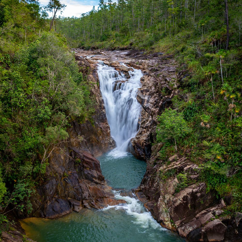 A cascading waterfall flows into a turquoise pool, surrounded by lush greenery and rocky cliffs.