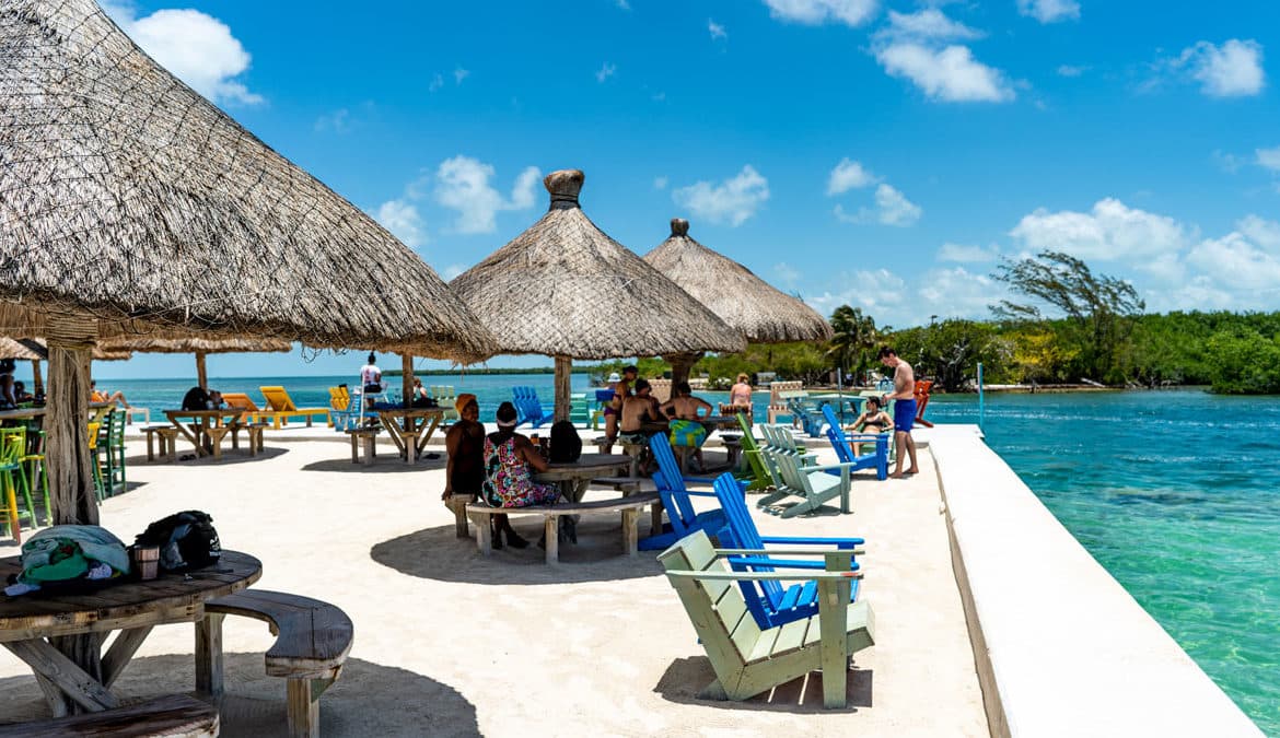 A vibrant beachside scene with thatched umbrellas and colorful chairs, where people gather by the turquoise water.