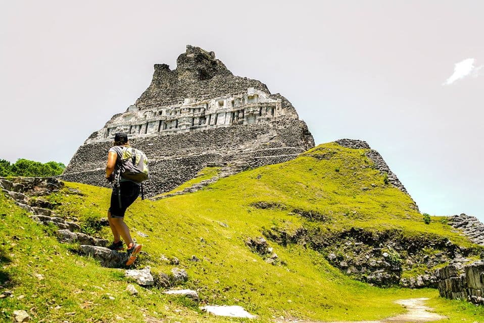 A hiker ascends stone steps towards a large, ancient structure on a grassy hill.