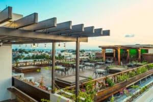 A rooftop terrace with wooden beams, seating areas, and greenery under a sunset sky.