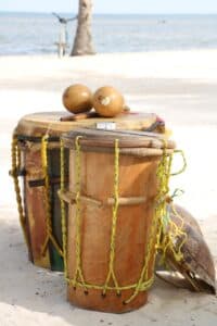 A set of drums and maracas on a sandy beach with an ocean backdrop.