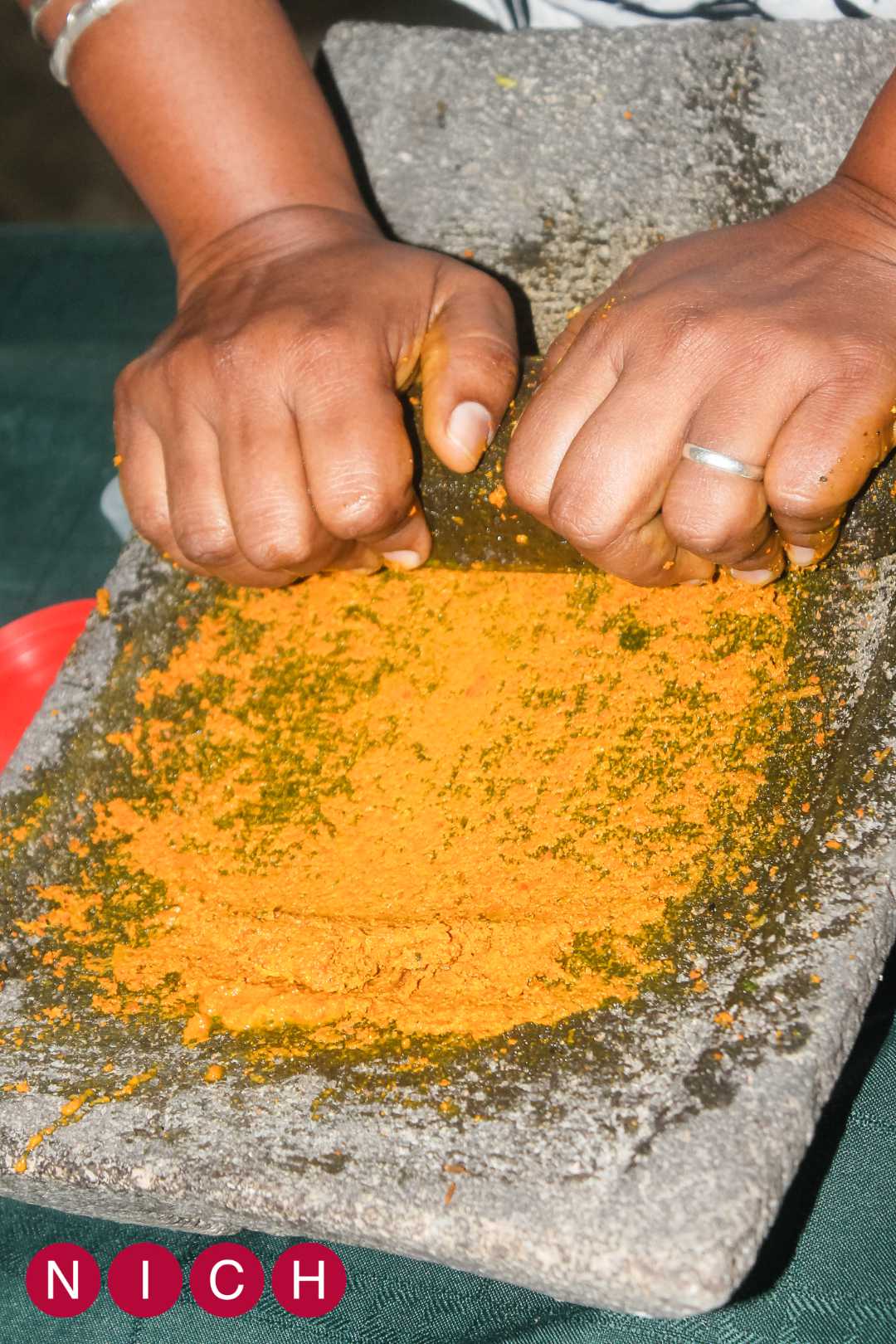 A person grinds spices on a stone mortar using their hands.