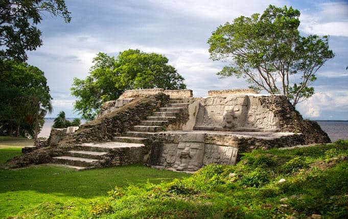 An ancient stone structure with carved faces, surrounded by lush greenery and trees.