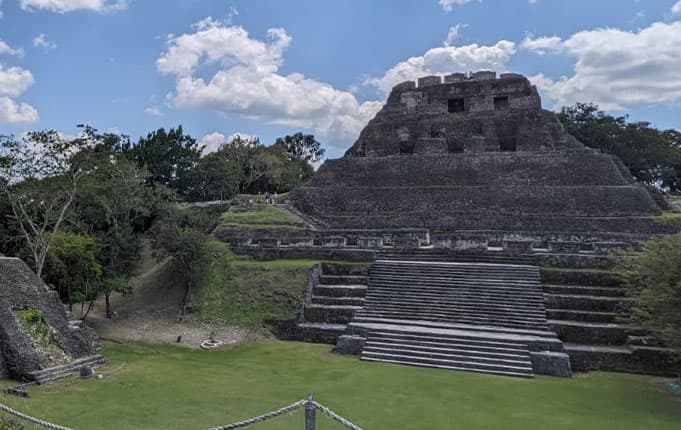 Ancient stone temple pyramid surrounded by lush greenery and a blue sky.