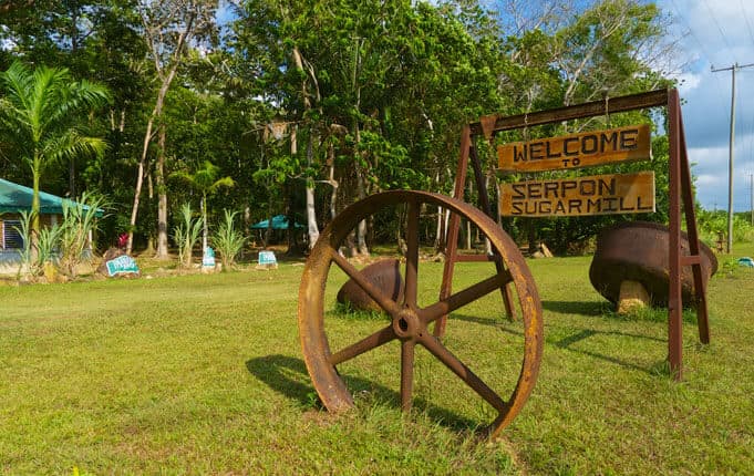 Sign welcoming visitors to Serpon Sugarmill with rustic wheels in the foreground.