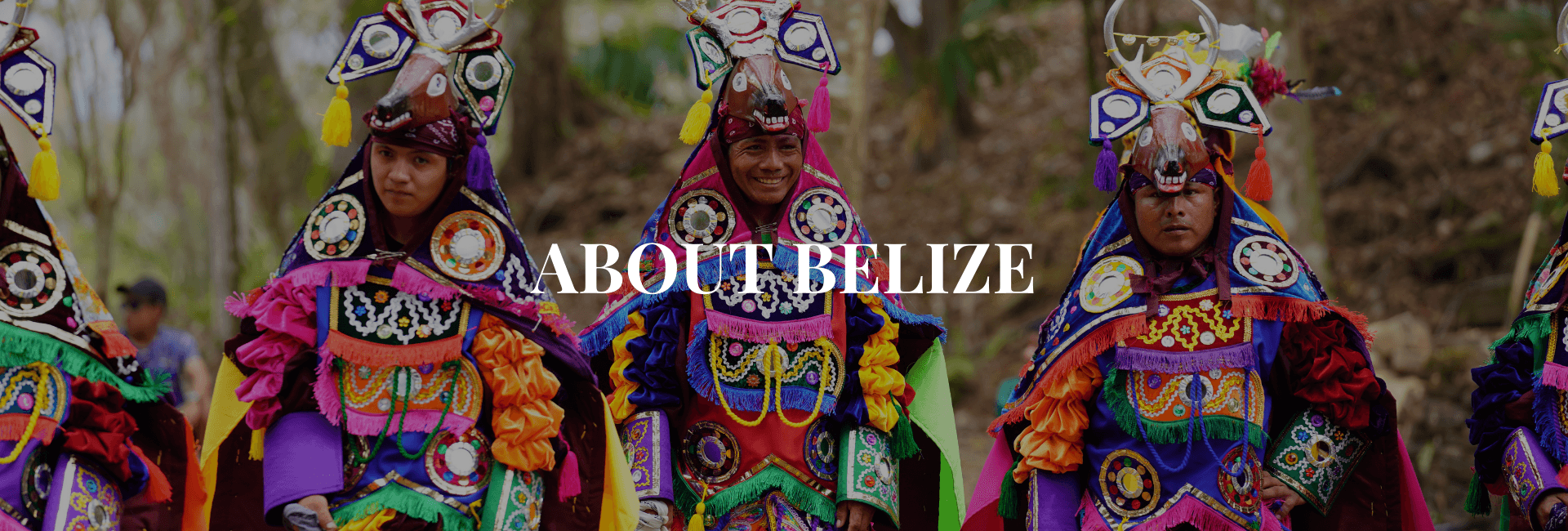 Four individuals dressed in vibrant traditional costumes stand together in a forested area.