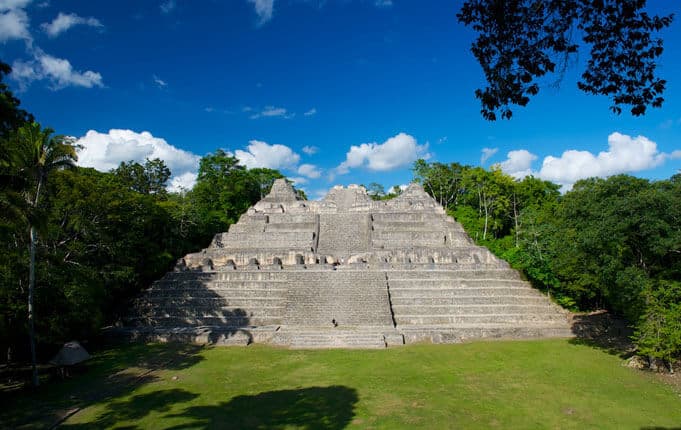 Ancient pyramid surrounded by dense jungle under a clear blue sky.