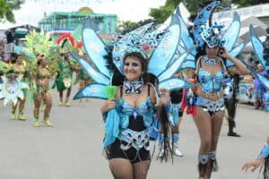 A woman in a vibrant butterfly costume dances at a festive parade, surrounded by others in colorful attire.