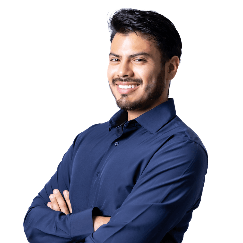 A smiling man in a dark blue shirt poses with his arms crossed against a white background.