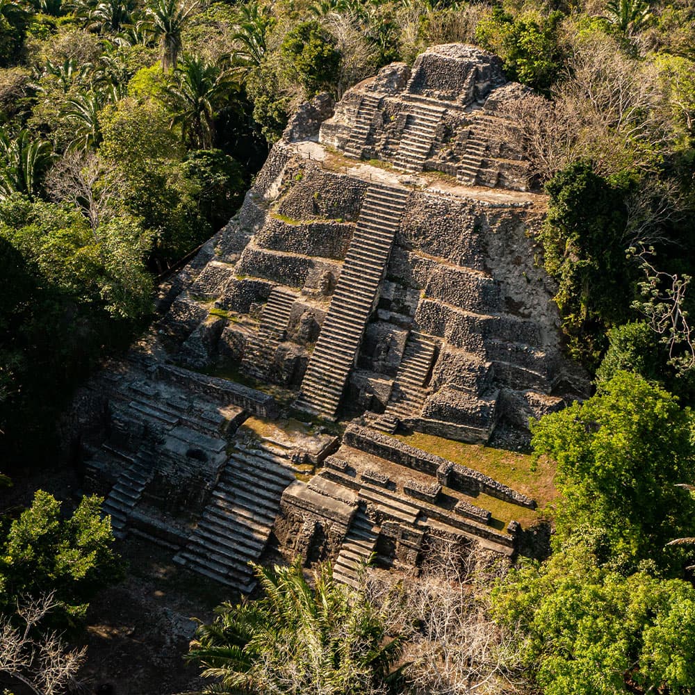 Aerial view of a stepped stone pyramid surrounded by lush greenery.
