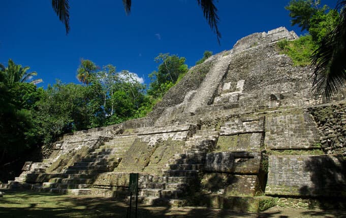 Ancient stone pyramid surrounded by lush greenery under a clear blue sky.