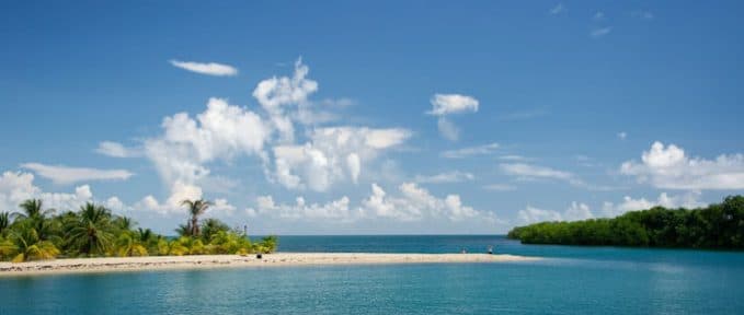 A serene tropical beach with clear blue water and fluffy clouds.