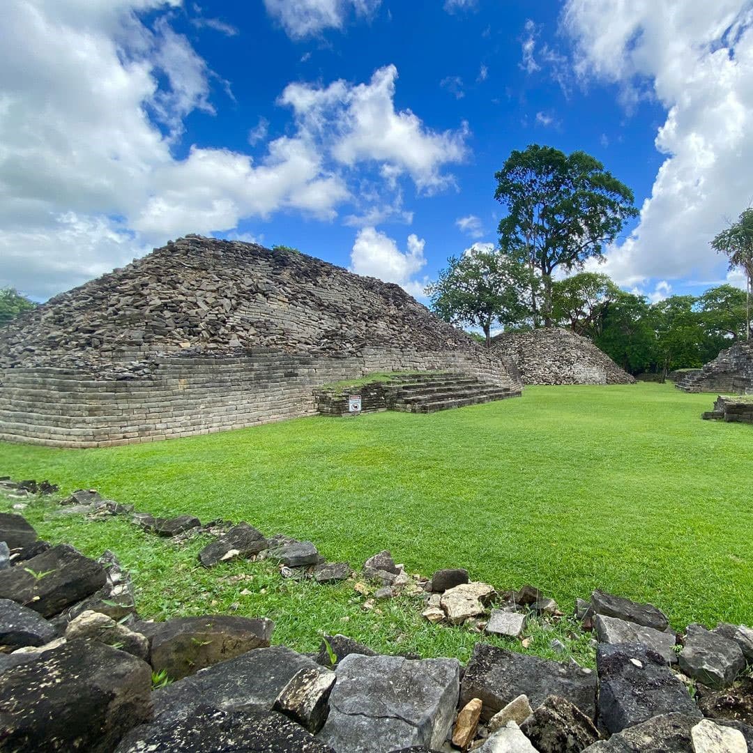 Ancient stone ruins surrounded by lush greenery under a blue sky.