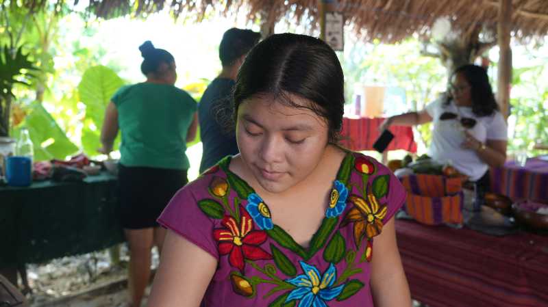A young girl in traditional clothing focuses on a task in a vibrant outdoor market setting.
